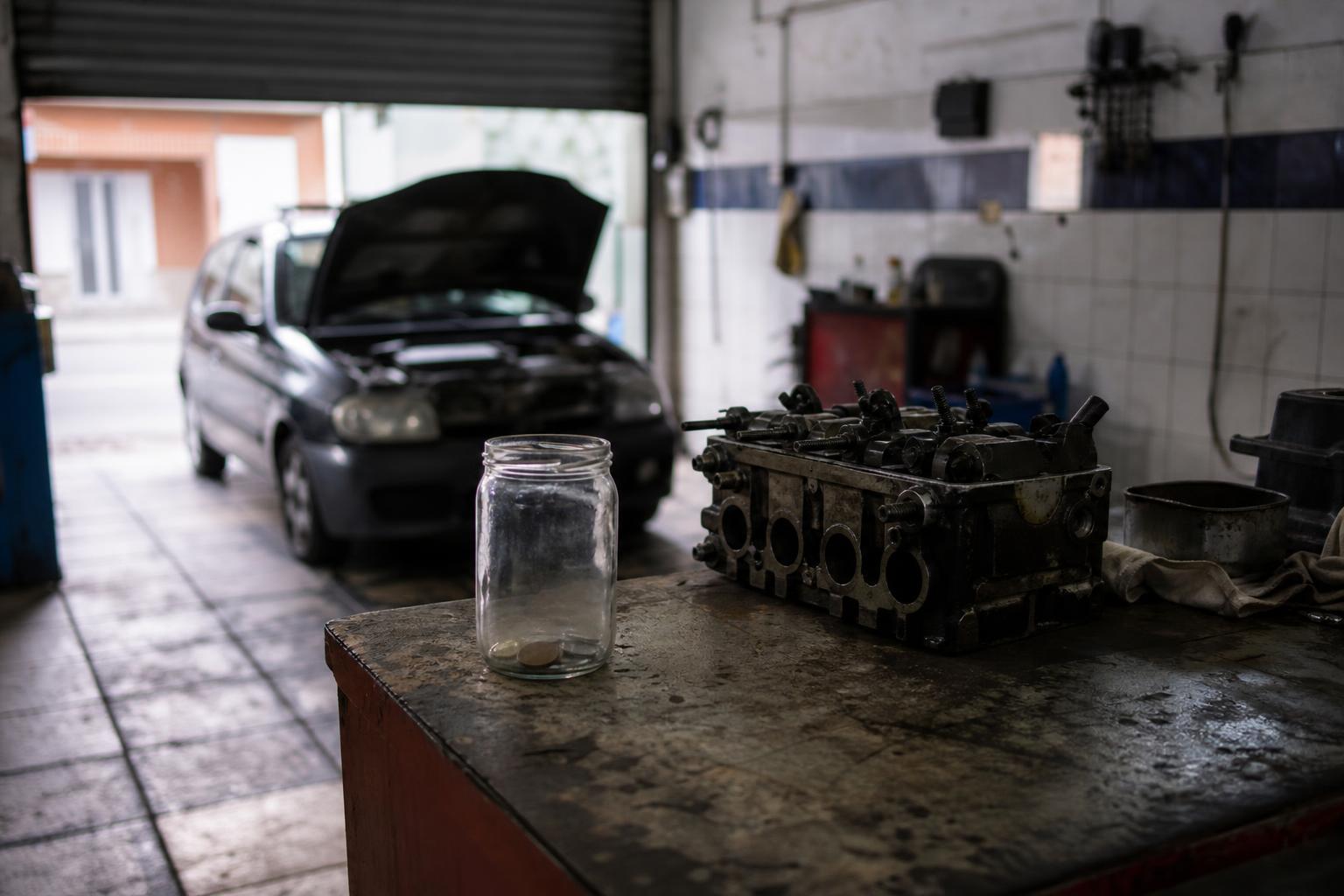 Un bote de cristal con unas pocas monedas junto a una pieza de motor sobre el mostrador de un taller.